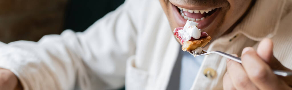oříznutý pohled na šťastného afroameričana, jak jí chutný dort v kavárně, banner - Fotografie, Obrázek