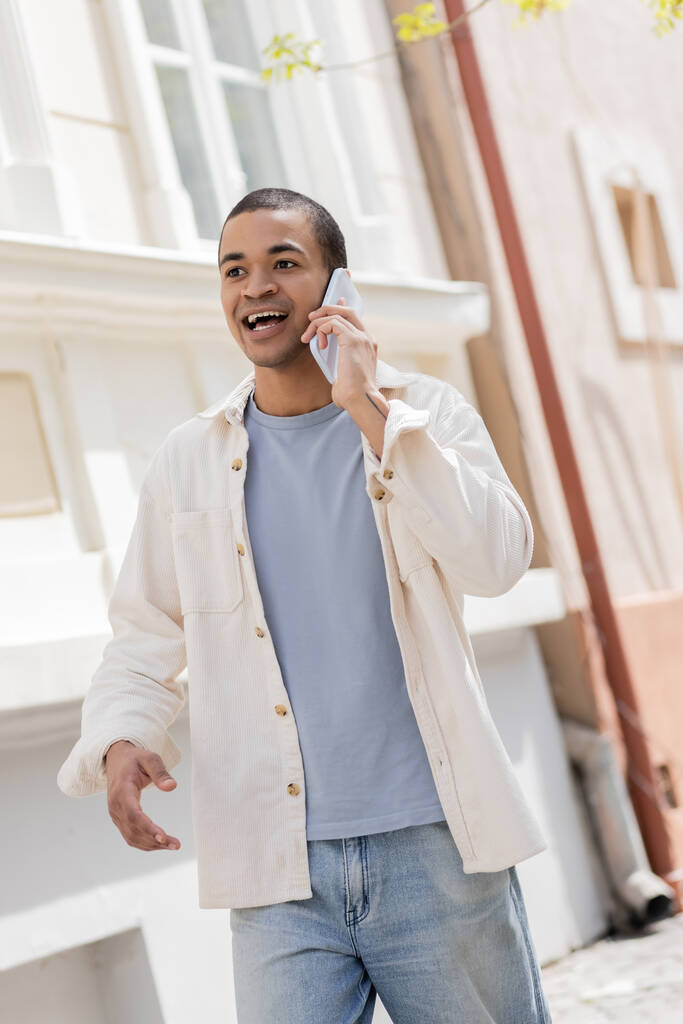 emocjonalny Afroamerykanin w koszuli mówi przez telefon komórkowy na ulicy w mieście  - Zdjęcie, obraz