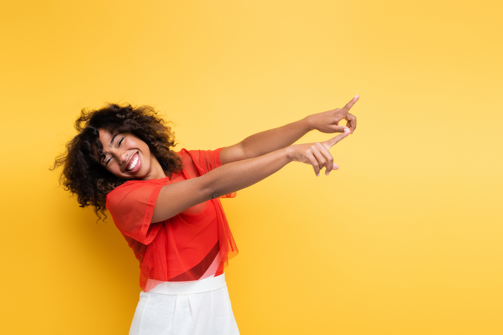 mujer afroamericana feliz en traje de verano señalando con los dedos aislados en amarillo - Foto, imagen