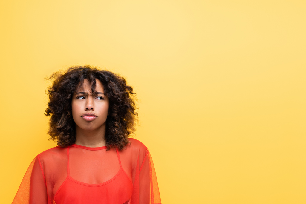 offensé afro-américaine en haut rouge boudant les lèvres et regardant loin isolé sur jaune - Photo, image