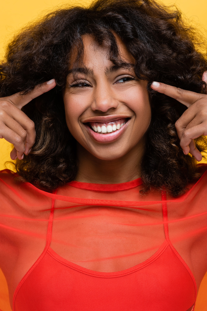 alegre afroamericana mujer apuntando con los dedos a sus ojos aislados en amarillo - Foto, Imagen