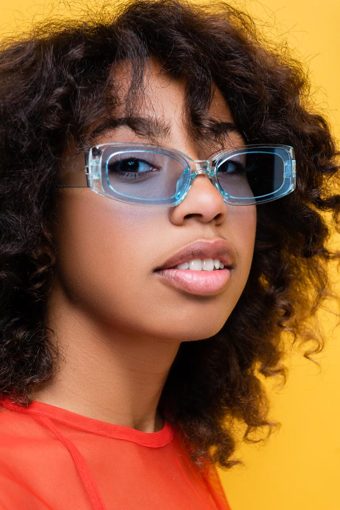 portrait de jolie femme afro-américaine aux lunettes de soleil bleues et tendance isolées sur jaune - Photo, image