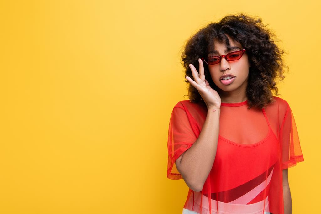 Kırmızı bluzlu modaya uygun Afro-Amerikalı kadın sarı gözlüklerini ayarlıyor. - Fotoğraf, Görsel