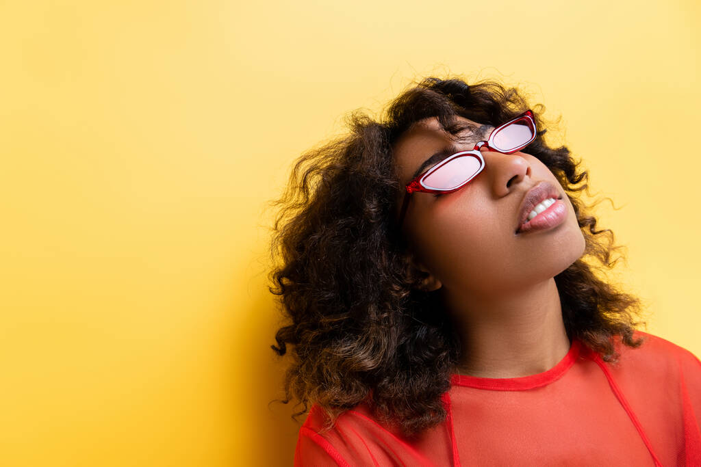 брюнетка африканська американка в модних сонцезахисних окулярах на жовтому тлі - Фото, зображення