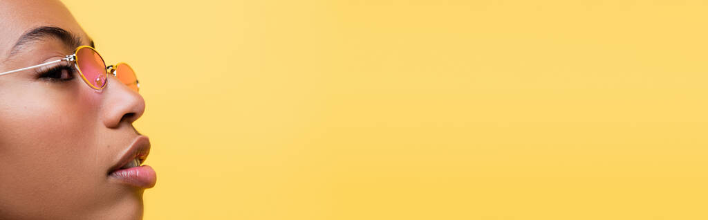 vista lateral de mujer afroamericana en gafas de moda aisladas en amarillo, pancarta - Foto, Imagen
