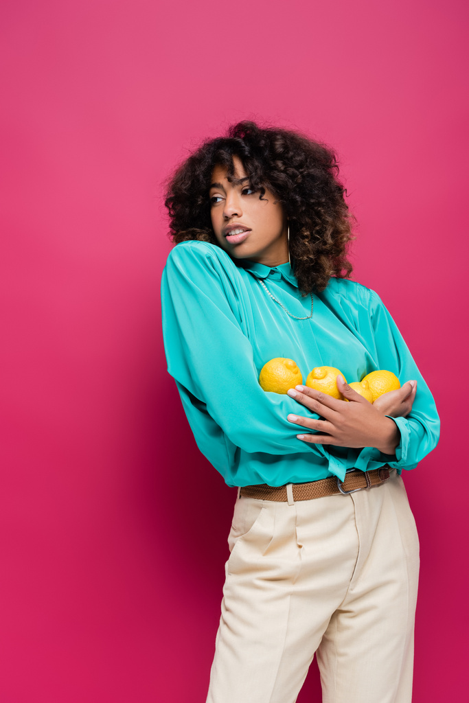 модна афроамериканська жінка з стиглими лимонами дивиться в сторону ізольовано на рожевому
 - Фото, зображення