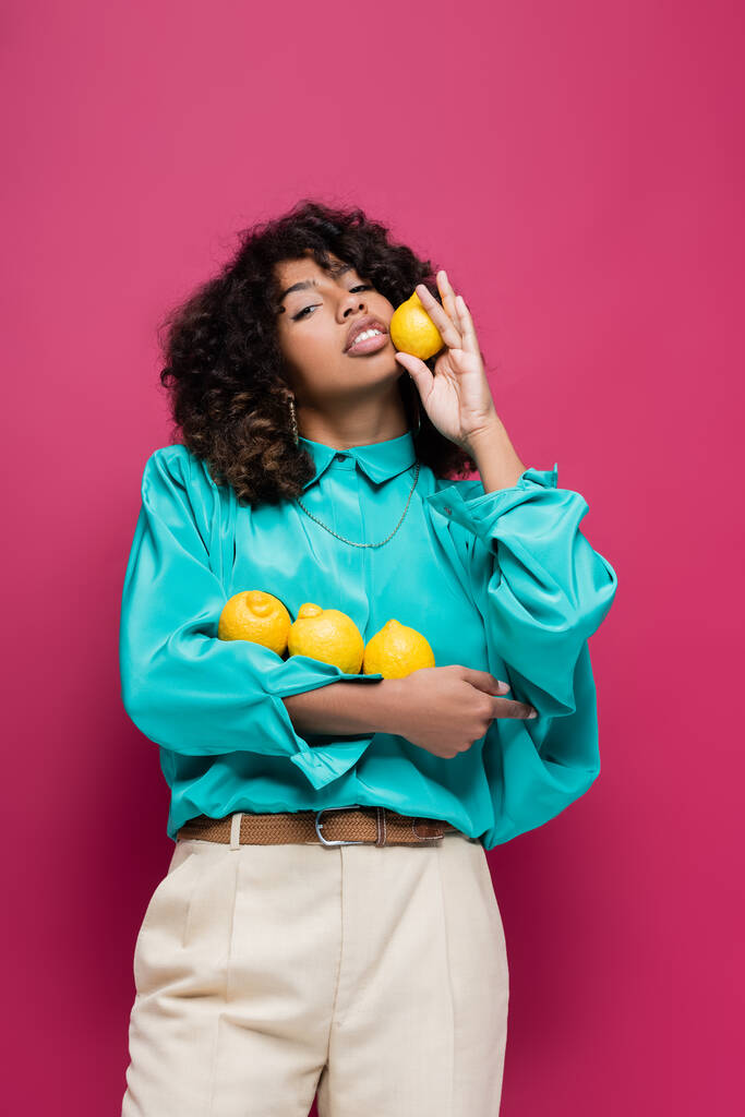hübsche afrikanisch-amerikanische Frau in trendiger Bluse mit Zitronen auf rosa - Foto, Bild
