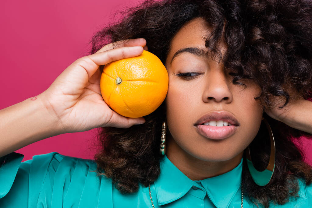 pretty african american woman holding ripe orange near face isolated on pink - Photo, Image