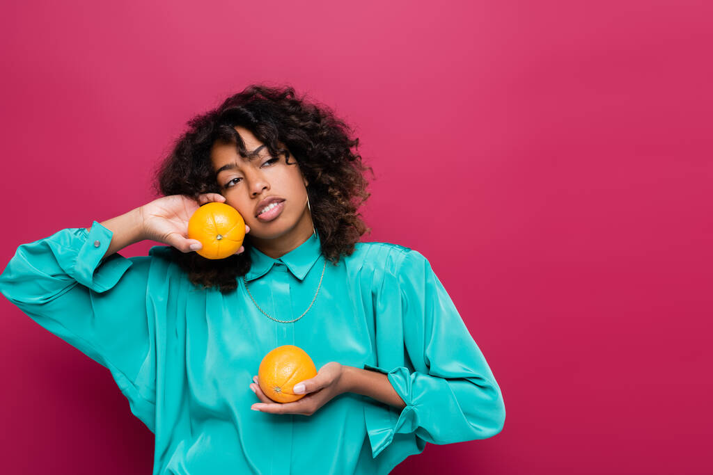 africká Američanka v tyrkysové blůze drží pomeranče a dívá se stranou izolované na růžové - Fotografie, Obrázek