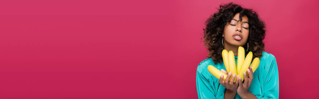 sensuale donna afroamericana ad occhi chiusi con banane mature isolate su rosa, striscione - Foto, immagini