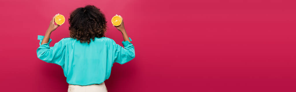 back view of curly african american woman with halves of ripe orange isolated on pink, banner - Photo, Image
