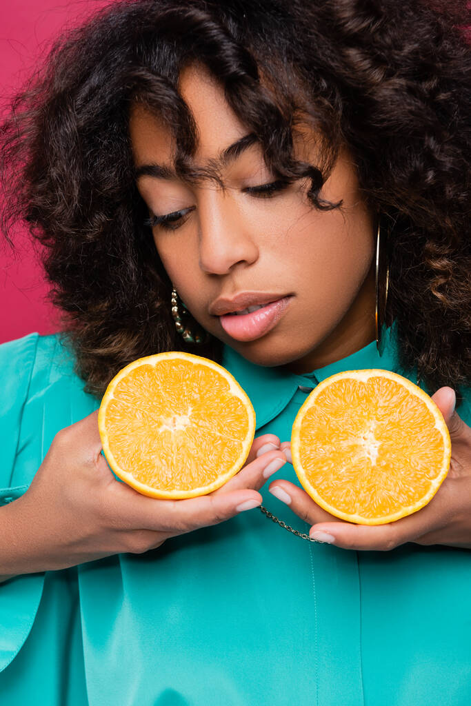 Африканская американка позирует с половинками сочного апельсина, изолированного на розовом - Фото, изображение