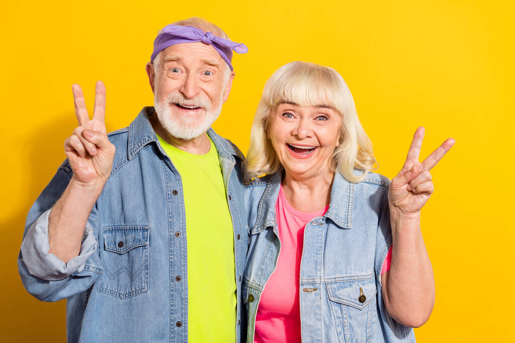 Fénykép izgatott barát barátnő nyugdíjas öltözött farmer ruha mutatja v-jelek izolált sárga színű háttér - Fotó, kép