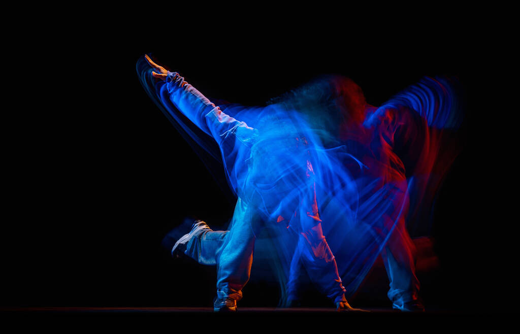 Tyylikäs mies tanssii hip-hop urheilullinen tyyli vaatteita eristetty tummalla taustalla tanssisalissa seka neon valoa. Nuorisokulttuuri, hip-hop, liike - Valokuva, kuva
