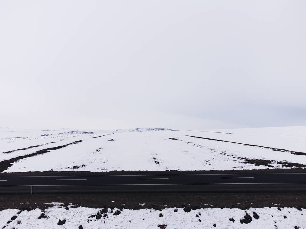 Πλευρική άποψη ενός πεπλατυσμένου δρόμου με κίτρινες λωρίδες και χιόνι το χειμώνα. - Φωτογραφία, εικόνα