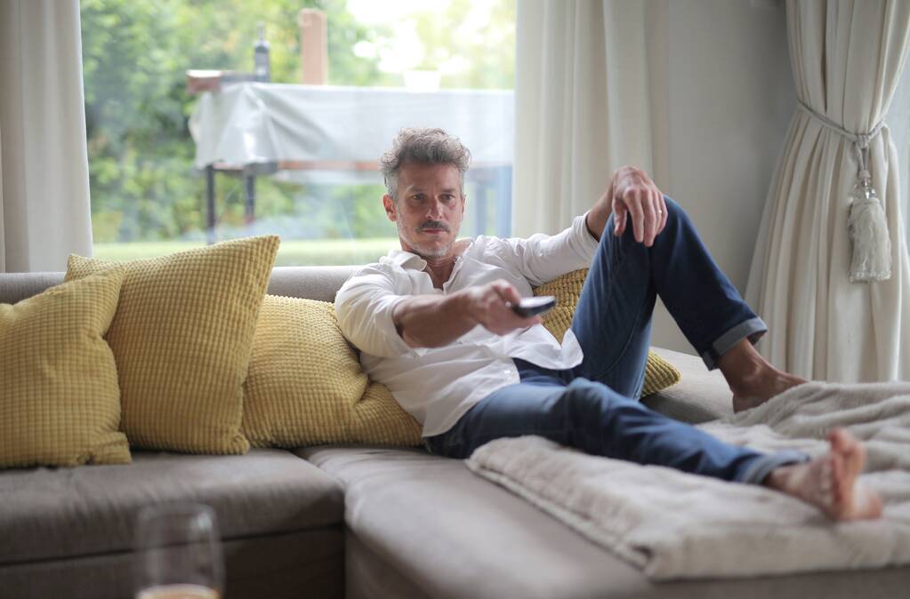 чоловік дивиться телевізор, сидячи на дивані вдома
 - Фото, зображення