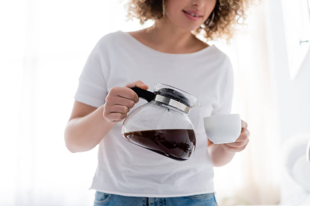 vista cortada de mulher encaracolado em branco t-shirt derramando café da manhã - Foto, Imagem