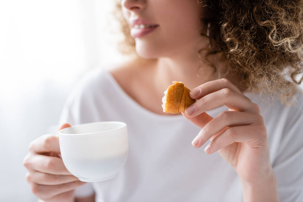 visão parcial da mulher desfocada com xícara de café e pedaço de croissant delicioso - Foto, Imagem