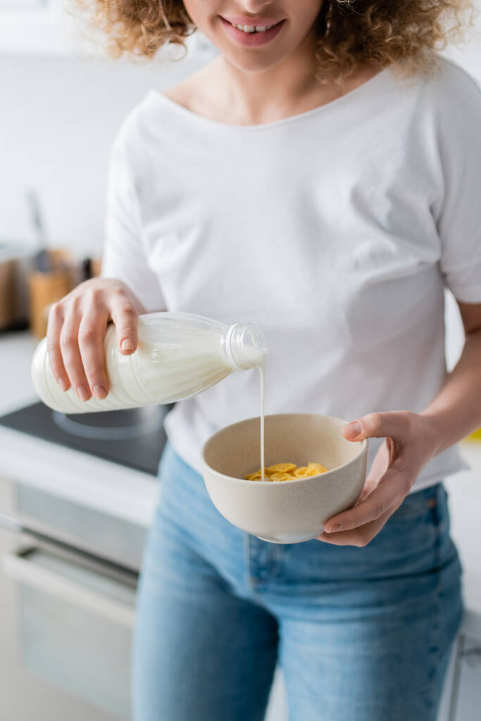 partial view of smiling woman pouring milk into bowl with tasty corn flakes - Photo, Image