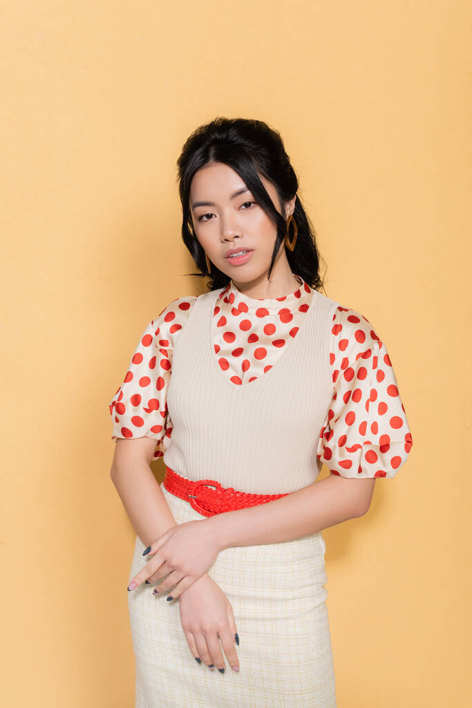 Portré stílusos ázsiai modell nézi kamera narancssárga háttér - Fotó, kép