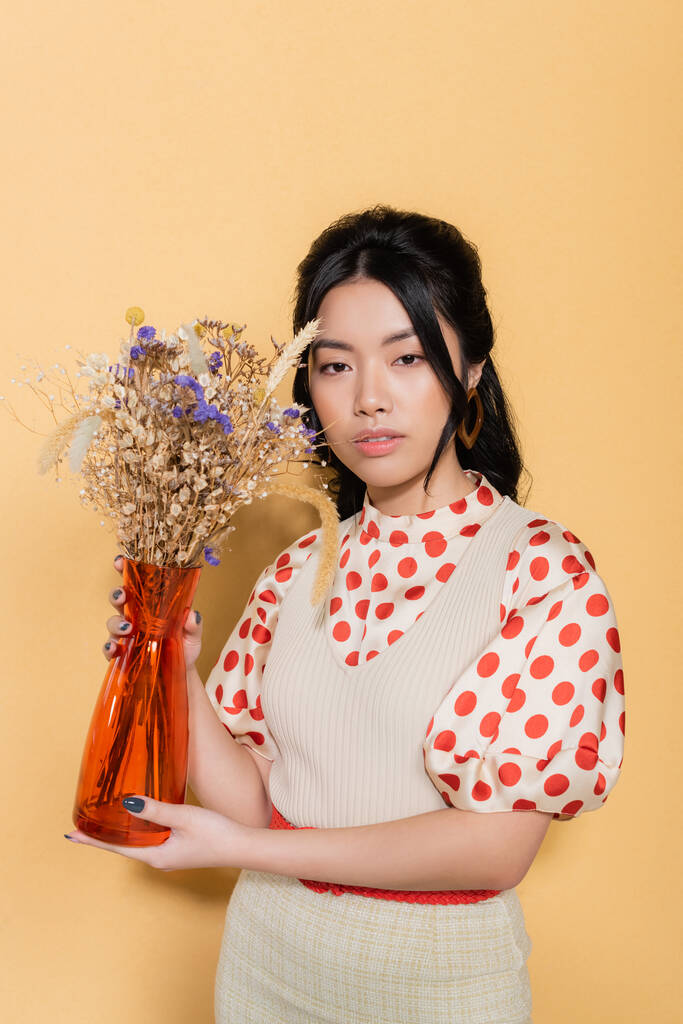 Elegante asiático modelo segurando vaso e flores no fundo laranja - Foto, Imagem