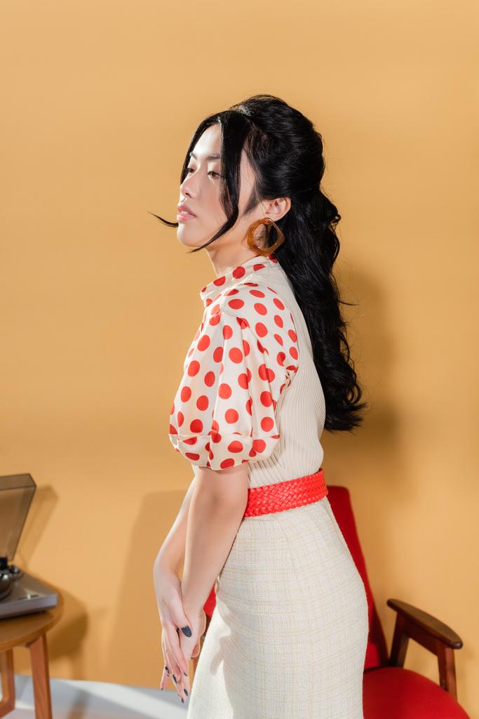 Junge asiatische Frau in Vintage-Klamotten schaut weg auf orangefarbenem Hintergrund - Foto, Bild
