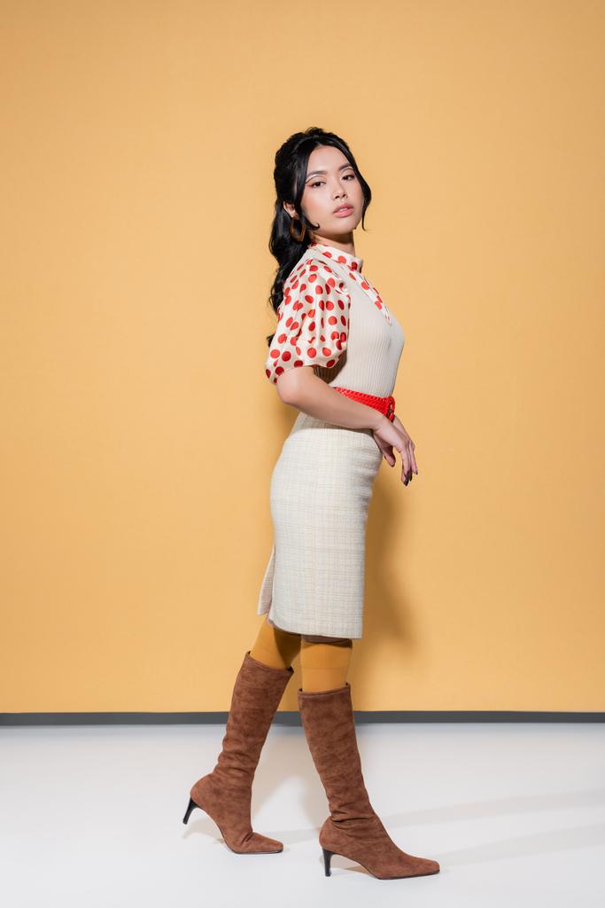 Mulher asiática bonita em blusa e vestido olhando para a câmera no fundo laranja - Foto, Imagem