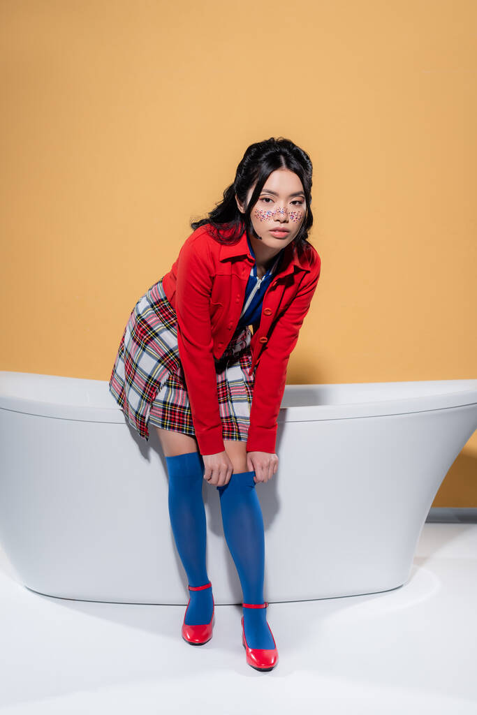 Aziatisch model aanpassen knie sok in de buurt van bad op oranje achtergrond - Foto, afbeelding