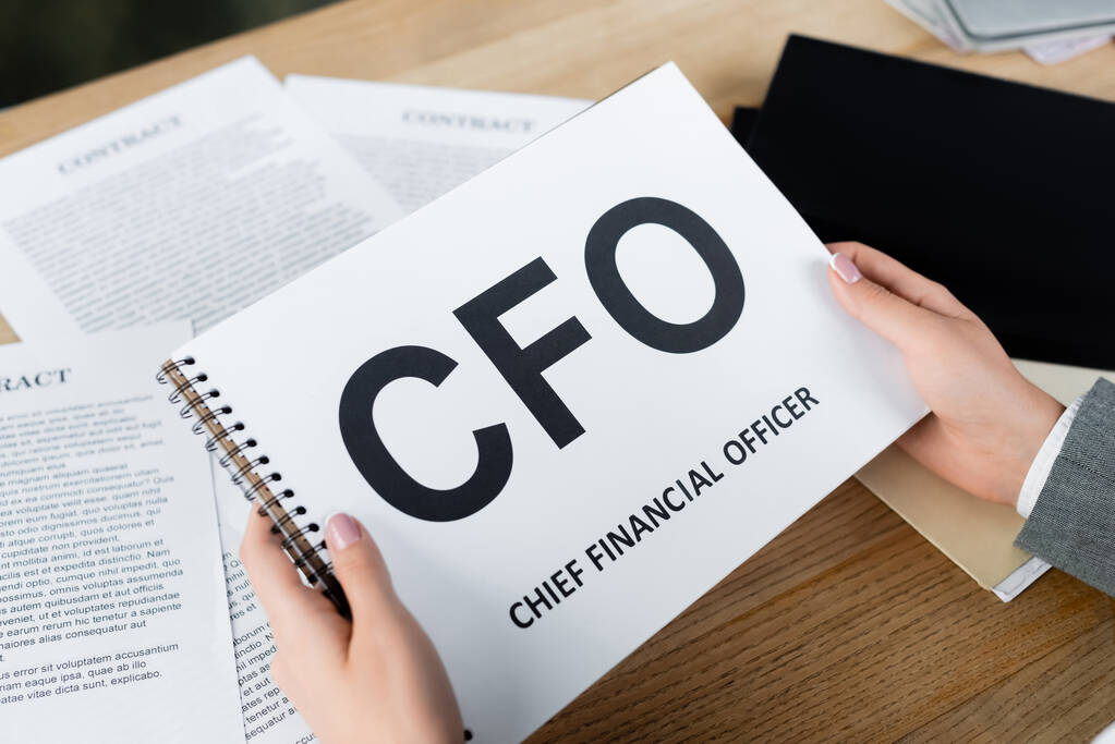 cropped view of businesswoman holding notebook with cfo lettering near blurred documents din office - Photo, Image