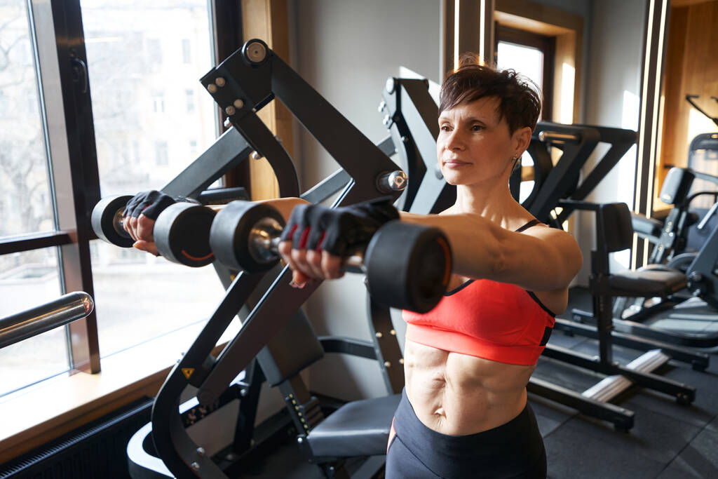 Soustředěný profesionální ženský atlet dělá činky vpředu zvýšit cvičení během silového tréninku - Fotografie, Obrázek