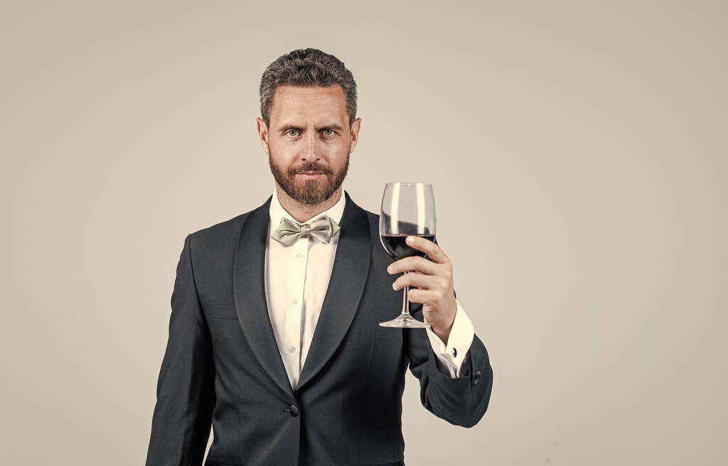 pohledný smoking muž jásot se sklenkou červeného vína držet dárkovou krabici za zády, kopírovací prostor, sommelier. - Fotografie, Obrázek