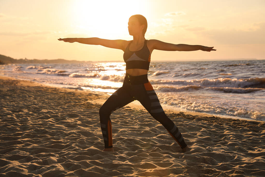Junges Mädchen macht Yoga am Strand bei Sonnenuntergang - Foto, Bild