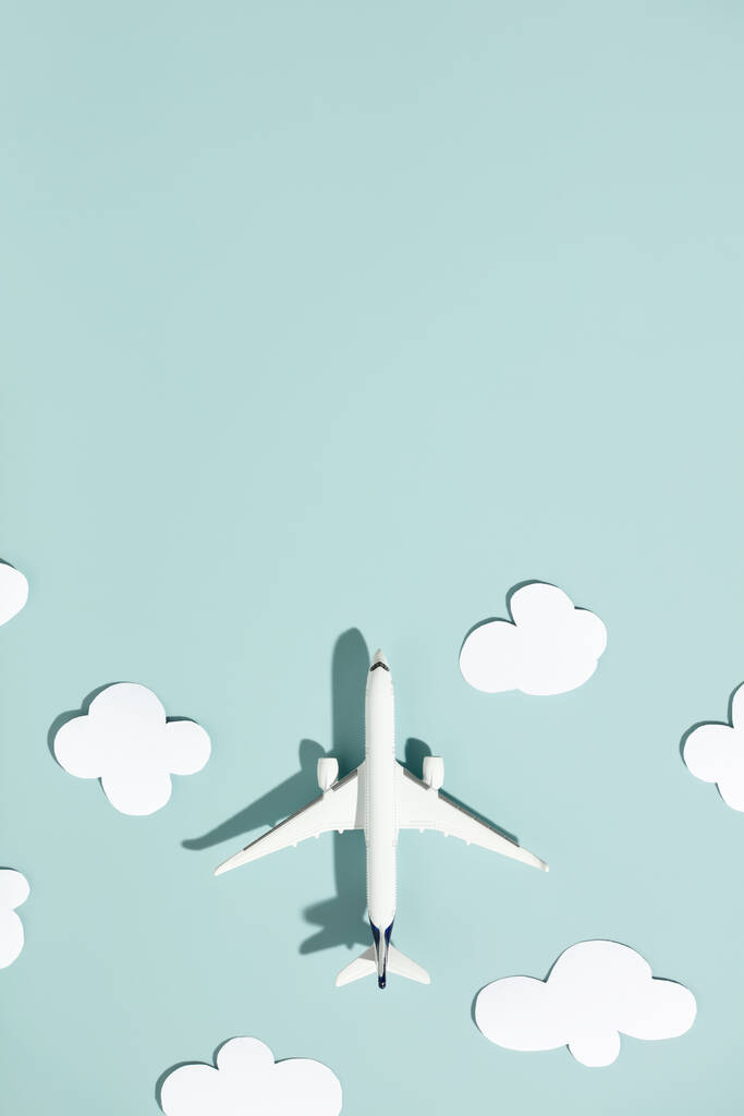 Avión de juguete en miniatura y nubes de papel sobre un fondo colorido. Viajes, vacaciones, turismo, aerolíneas, concepto de vuelos de bajo costo. Vista superior, plano. - Foto, imagen