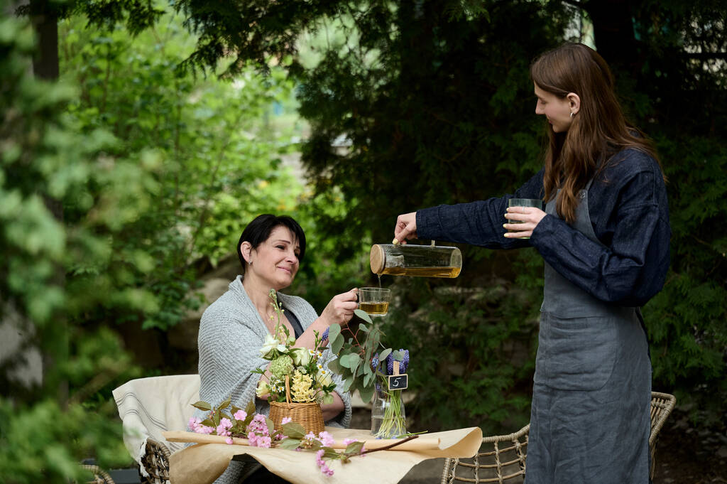 İki çiçekçi anne ve kızı bahçede çay içiyorlar. - Fotoğraf, Görsel