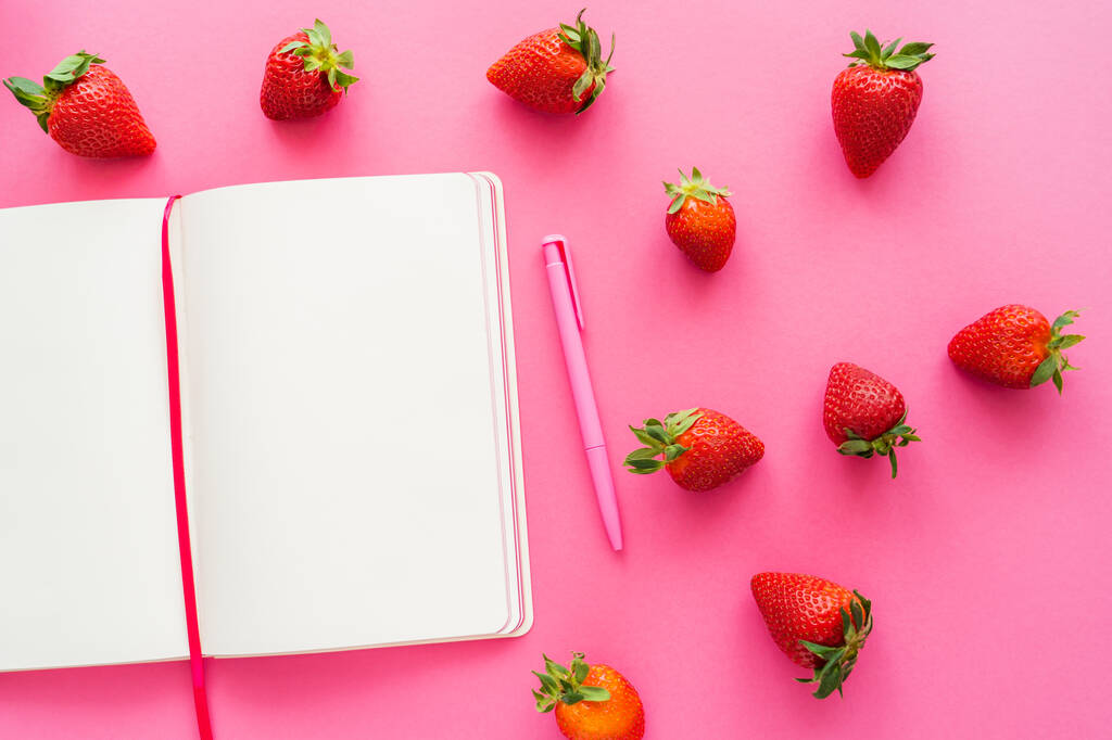 Vista superior de fresas orgánicas y cuaderno abierto sobre fondo rosa  - Foto, Imagen