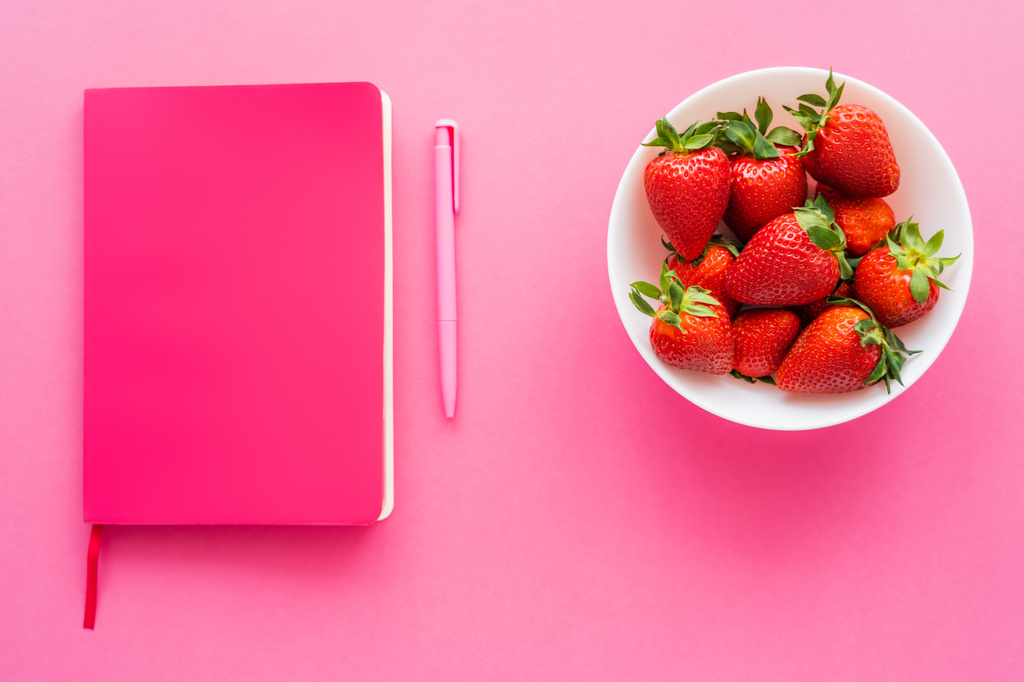 Notizbuch in der Nähe von Stift und ganzen Erdbeeren in Schale auf rosa Hintergrund  - Foto, Bild