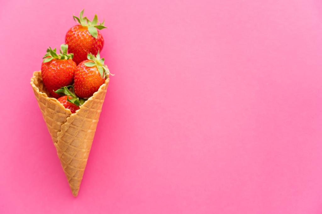 Draufsicht auf frische Erdbeeren in Waffelkegel auf rosa Hintergrund  - Foto, Bild