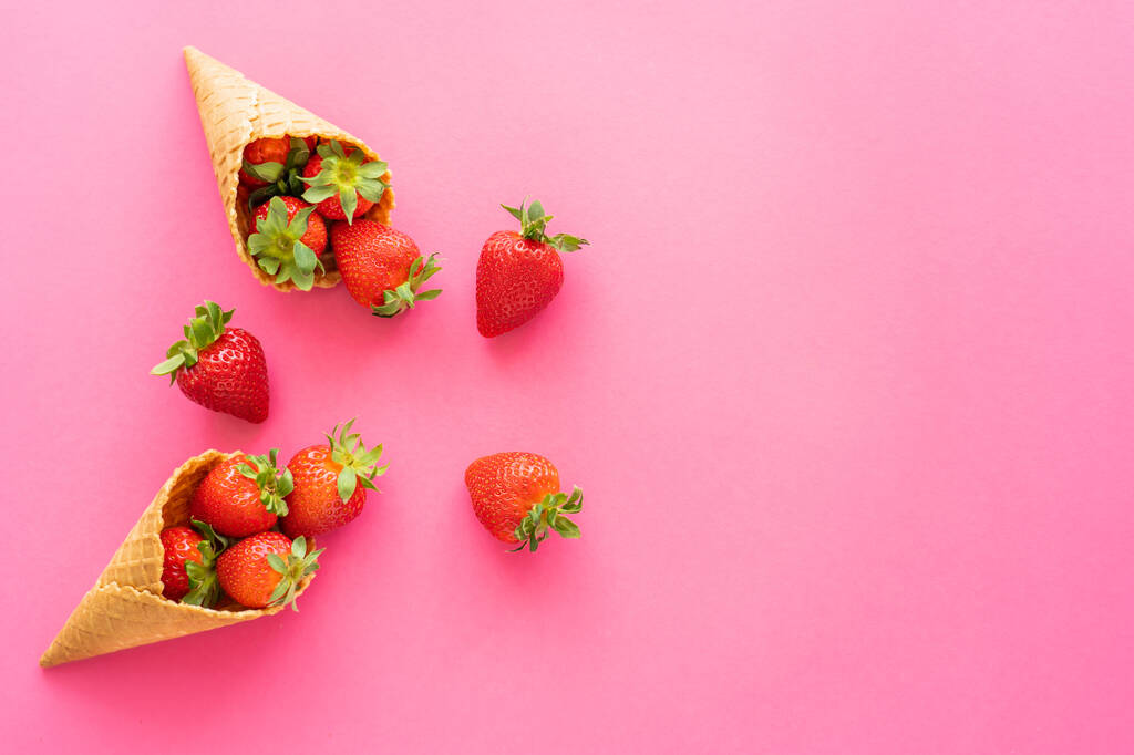 Draufsicht auf saftige Erdbeeren in süßen Waffelkegeln auf rosa Hintergrund  - Foto, Bild