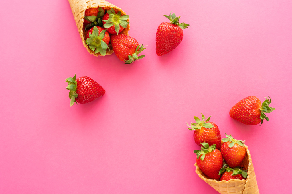 Top view of fresh strawberries with leaves in waffle cones on pink background  - Photo, Image