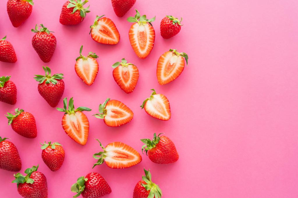 Flache Lage mit rotem Schnitt und ganzen Erdbeeren auf rosa Hintergrund  - Foto, Bild