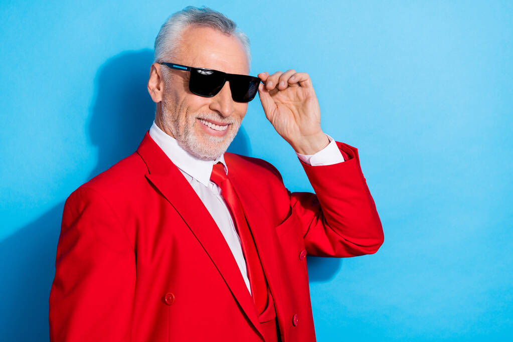 Foto de alegre executivo ceo aposentado homem brilhante sorriso desgaste sol vermelho smoking isolado azul cor fundo. - Foto, Imagem