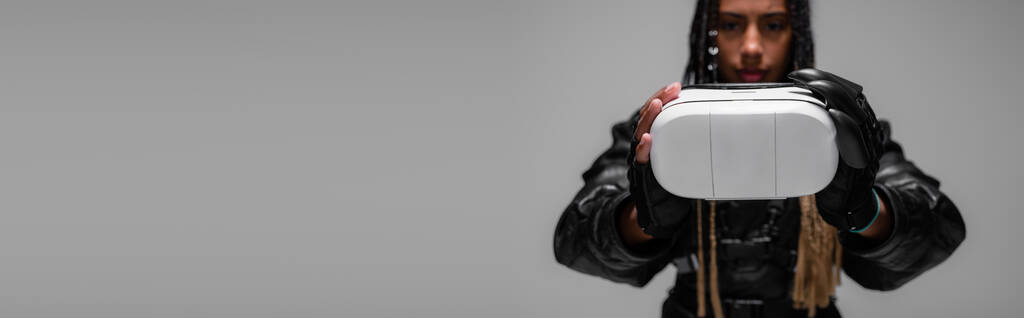 Розмита афріканська жінка в шкіряній куртці з навушниками ізольовані на сірому банері.  - Фото, зображення