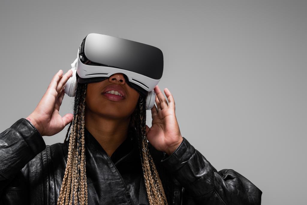 African american woman in vr headset listening music in headphones isolated on grey  - Photo, Image