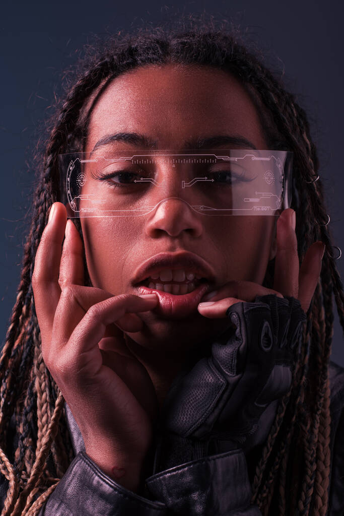 Retrato de mulher afro-americana de luva e óculos inteligentes olhando para a câmera isolada em cinza escuro  - Foto, Imagem