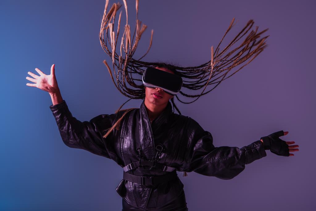 Stylish african american woman with pigtails using vr headset on blue and purple background  - Photo, Image