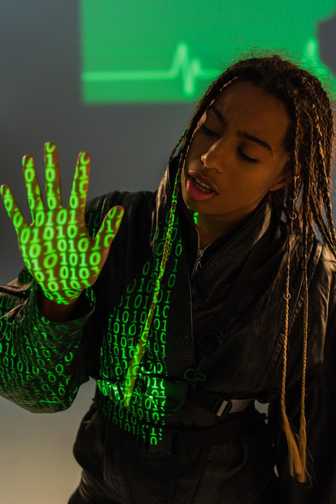 Afrikkalainen amerikkalainen nainen nahkatakki kanssa projektio tietokoneen koodi harmaalla pohjalla  - Valokuva, kuva