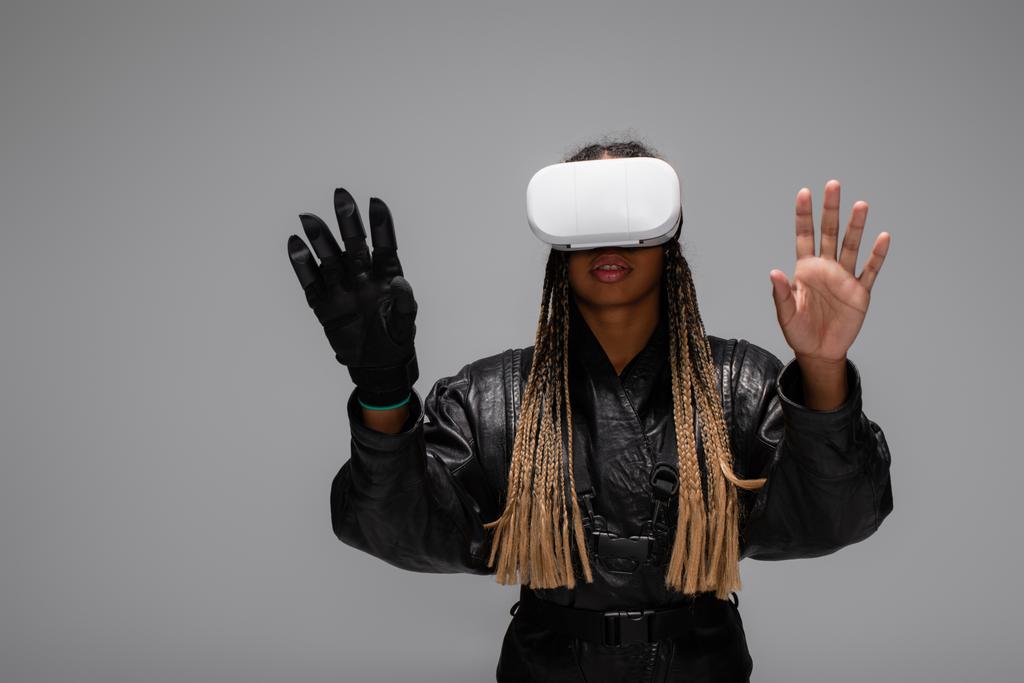 Afričanky americká žena ve vr sluchátka a kybernetické rukavice hry izolované na šedé  - Fotografie, Obrázek