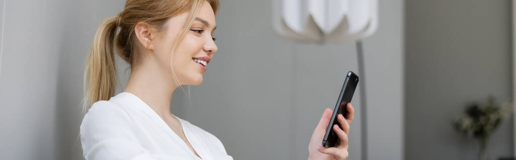 Jeune femme positive en chemisier utilisant un téléphone portable à la maison, bannière  - Photo, image