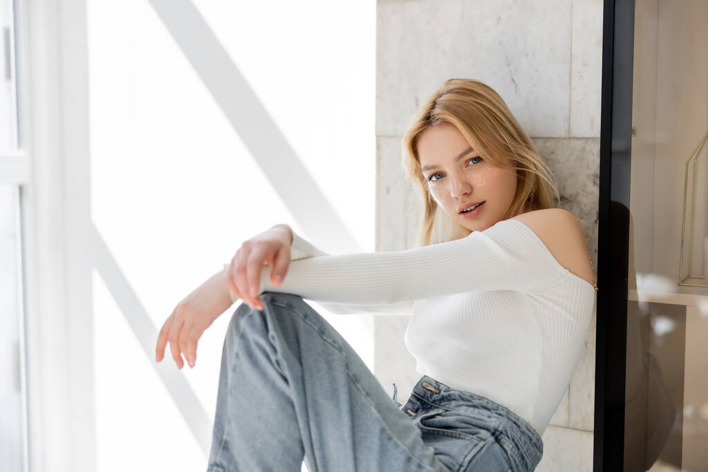 jong blond vrouw in jeans kijken naar camera thuis  - Foto, afbeelding