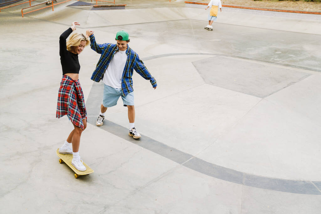 Amis multiraciaux riant tout en chevauchant dans un skate park le jour d'été - Photo, image